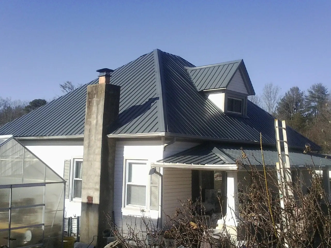 Dark blue standing seam metal roof on a white farmhouse with dormer — Slate & Tile Roof Repair by Roofing Brothers in Loveland
