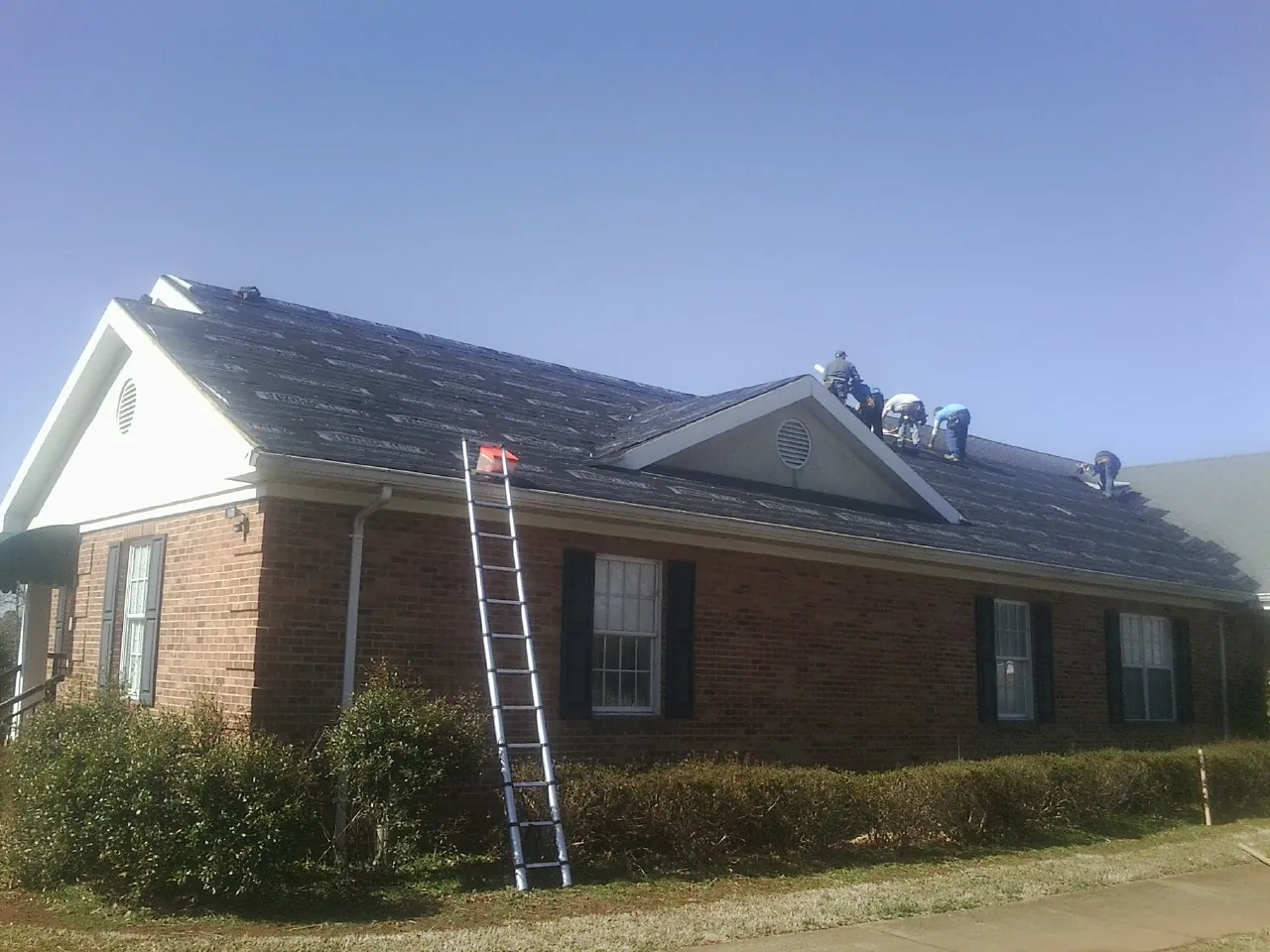 Crew tearing shingles off a brick ranch roof with a ladder set — Metal Roof Repair work by our crew in Loveland