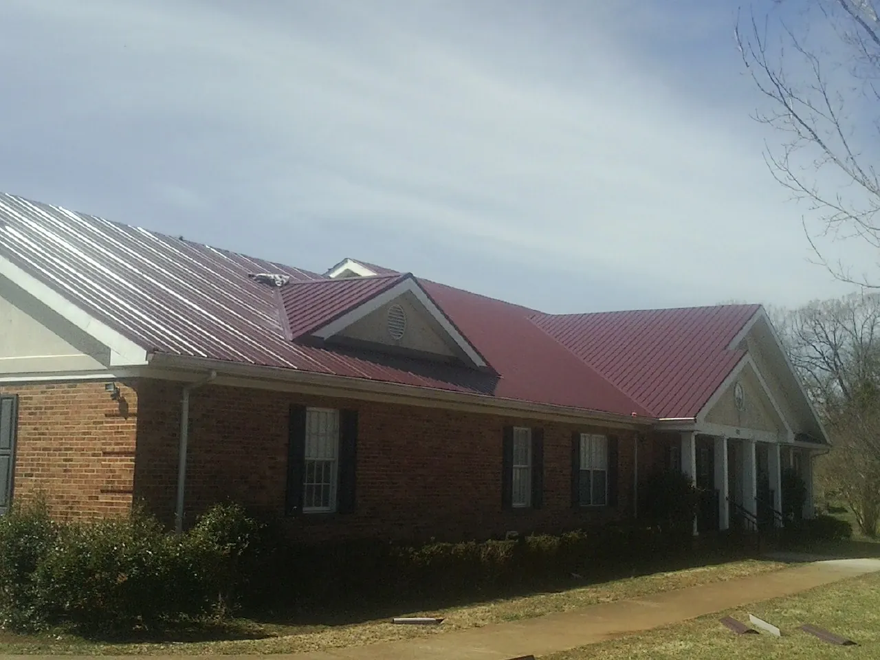 Red metal roof with gabled entries on a long brick building, from a Hail Damage Roof Repair job in Loveland