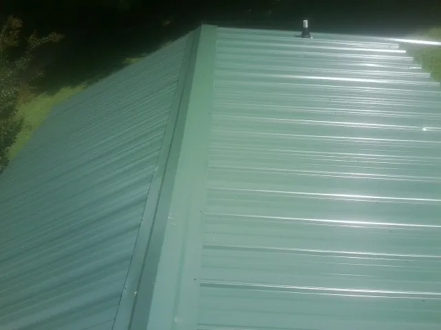 New green metal panels meeting at the ridge of a roof — Flat Roof Repair work by our crew in Loveland