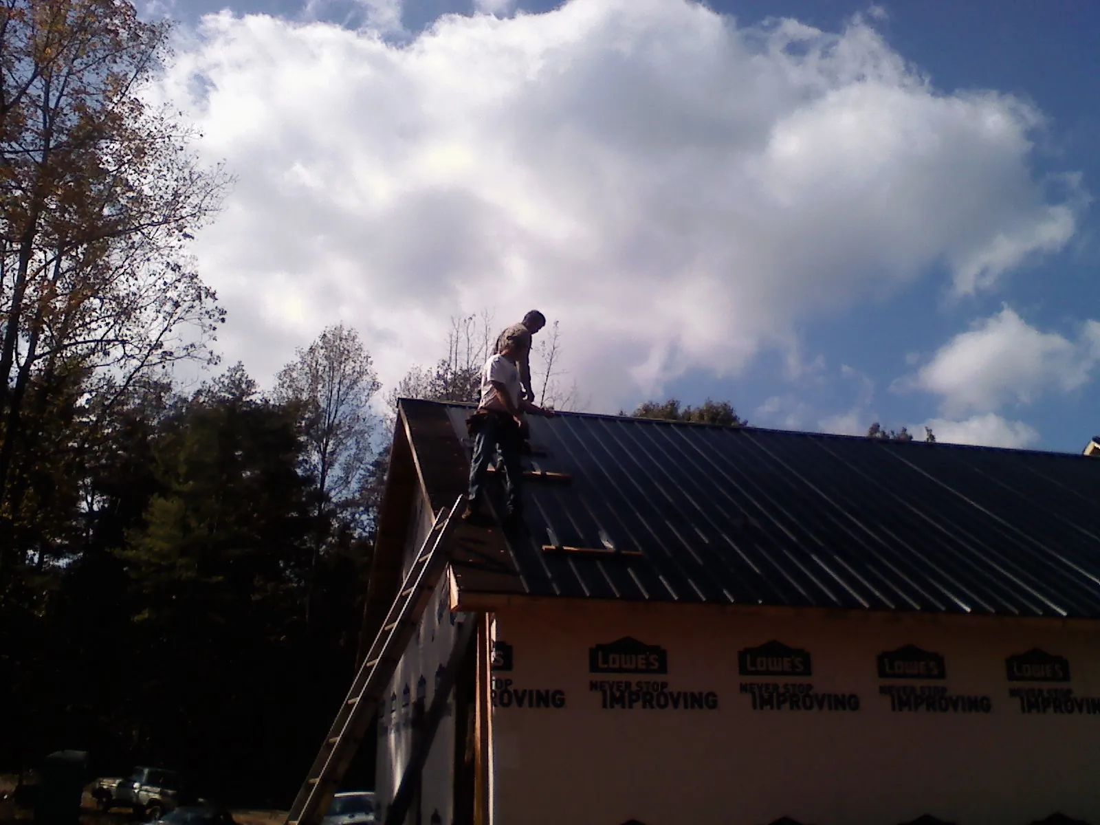 Roofer fastening dark metal panels high against a cloudy sky, from a Roof Inspection job in Loveland