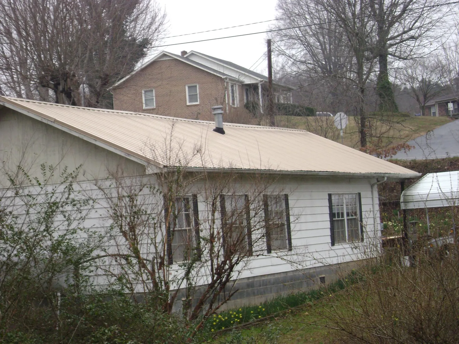 Tan metal roof on a white sided house set into a hillside — Commercial Roofing by Roofing Brothers in Loveland